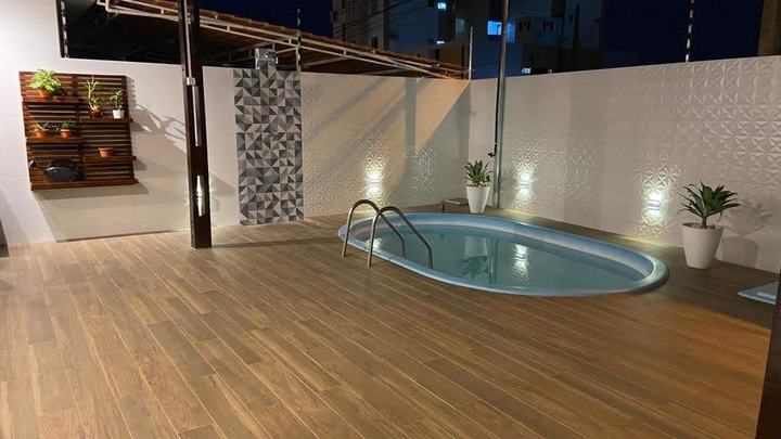 Área de lazer com piscina, piso amadeirado e parede revestida, iluminada à noite