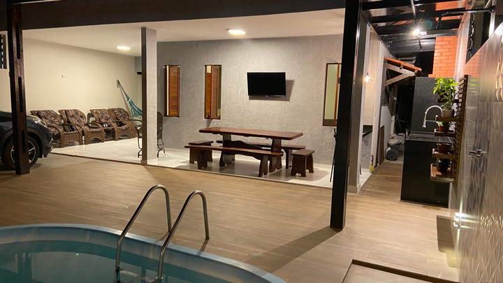 Área gourmet com mesa de madeira e TV, integrada à piscina