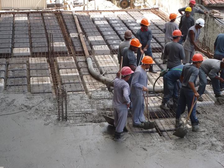 Equipe com capacetes fazendo a concretagem de uma laje